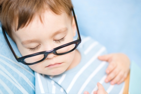 Cute little boy is sleeping while wearing glasses and put off his bookの写真素材