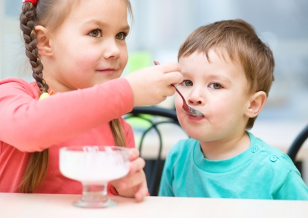 Girl is feeding his little brother with ice-cream in parlorの写真素材