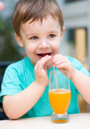 Little boy is drinking orange juice using strawの写真素材