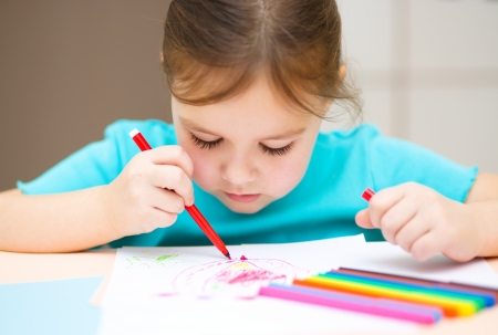 Cute cheerful child drawing using felt-tip pen while sitting at tableの写真素材