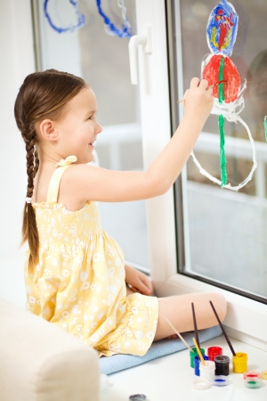 Portrait of a cute cheerful girl playing with paints on windowの写真素材
