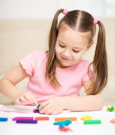 Little girl is playing with plasticine while sitting at tableの写真素材