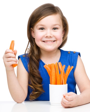 Cute little girl is eating carrot, isolated over whiteの写真素材
