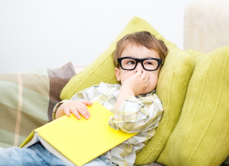 Little boy is reading book while laying on couch, indoor shootの写真素材