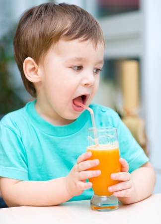 Little boy is drinking orange juice using strawの写真素材