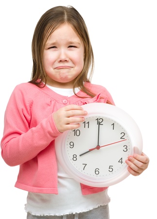 Little girl is holding big clock and showing unhappy grimace, isolated over whiteの写真素材