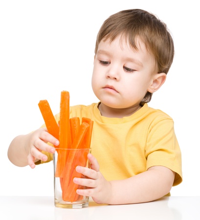 Little boy is eating carrot, isolated over whiteの写真素材