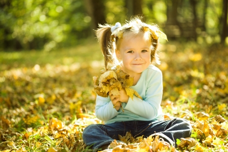Cute little girl in autumn park holding bunch of yellow leavesの写真素材