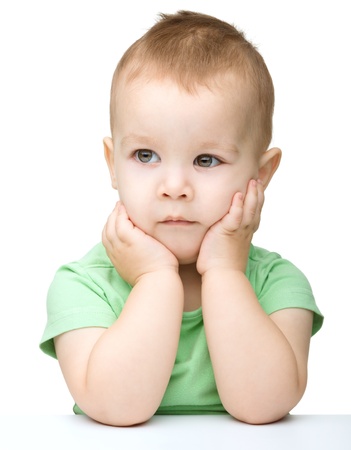 Portrait of a cute little boy sitting at table supporting his head with hand, isolated over whiteの写真素材