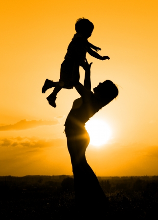 Silhouette of mother playing with her son backlit by sunsetの写真素材