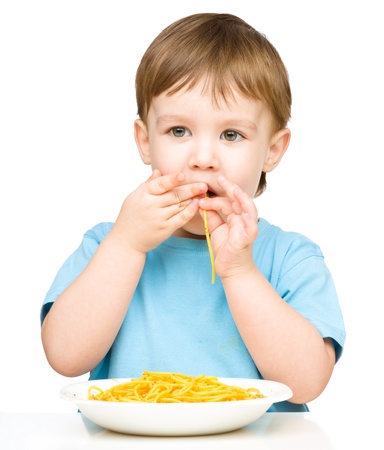 Little boy is eating spaghetti using both hands, isolated over whiteの写真素材