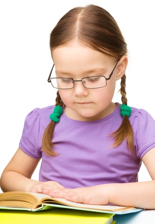 Cute little girl is reading a book while wearing glasses, isolated over whiteの写真素材