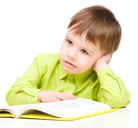 Cute little child play with book while sitting at table, isolated over whiteの写真素材