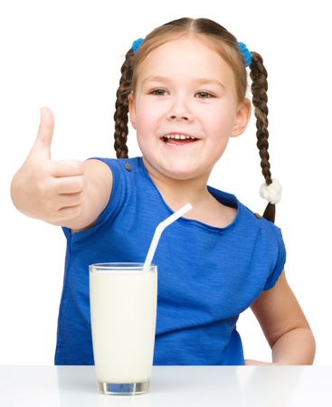 Cute little girl drinks milk using a drinking straw while showing thumb up sign, isolated over whiteの写真素材
