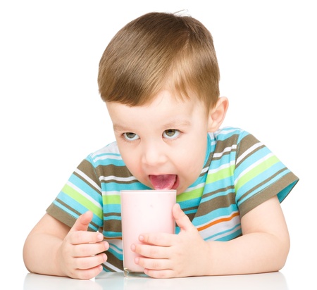 Cute little boy is dipping his tongue in the glass of milk, isolated over whiteの写真素材