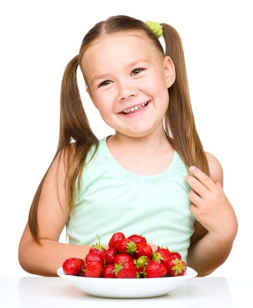 Cheerful little girl is eating strawberries, isolated over whiteの写真素材