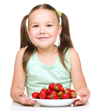 Cheerful little girl is eating strawberries, isolated over whiteの写真素材