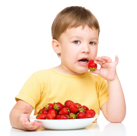 Little boy is eating strawberries, isolated over whiteの写真素材
