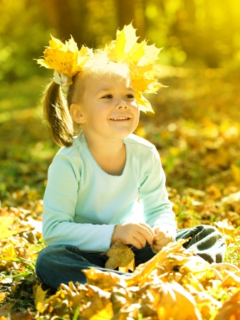 Cute little girl in autumn park holding bunch of yellow leavesの写真素材