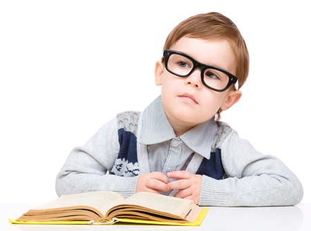 Cute little child play with book and wearing glasses while sitting at table, isolated over whiteの写真素材