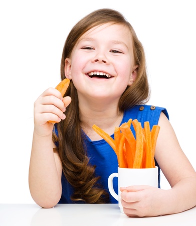 Cute little girl is eating carrot, isolated over whiteの写真素材