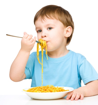 Little boy is eating spaghetti using fork, isolated over whiteの写真素材
