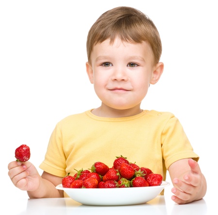 Little boy is eating strawberries, isolated over whiteの写真素材