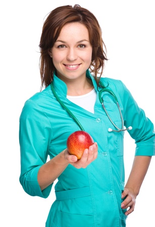 Young lady doctor is holding a red apple, isolated over whiteの写真素材