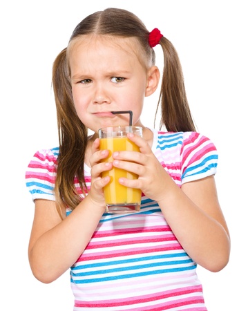 Little girl unwillingly drinking orange juice using straw, isolated over whiteの写真素材