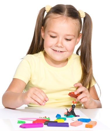 Little girl is playing with plasticine while sitting at table, isolated over whiteの写真素材