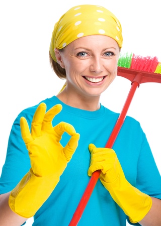 Young woman as a cleaning maid holding broom and showing OK sign, isolated over whiteの写真素材