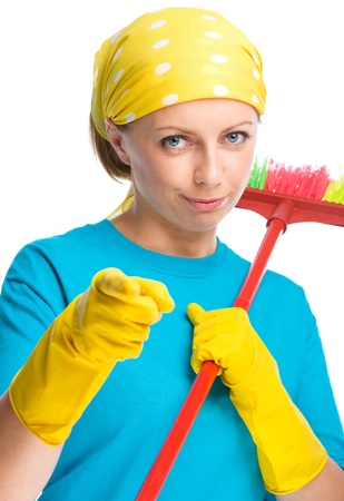 Young woman as a cleaning maid holding broom and pointing on you, isolated over whiteの写真素材
