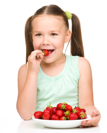 Happy little girl eats strawberries and shows the thumb up sign, isolated over whiteの写真素材