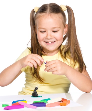 Little girl is playing with plasticine while sitting at table, isolated over whiteの写真素材
