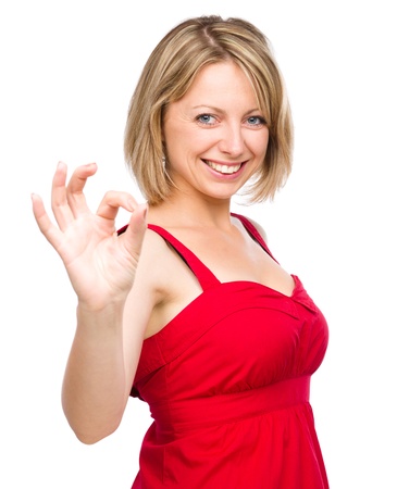 Young woman dressed in red is showing OK sign, isolated over whiteの写真素材