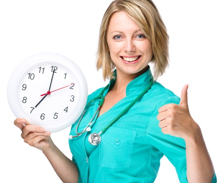 Young happy lady doctor is holding clock showing seven, isolated over whiteの写真素材