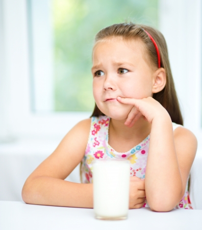 Sad little girl refuses to drink a glass of milkの写真素材