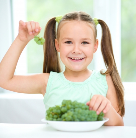 Cute little girl is eating green grapes, isolated over whiteの写真素材
