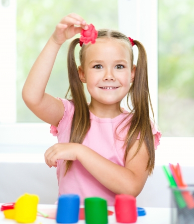 Little girl is playing with plasticine while sitting at tableの写真素材