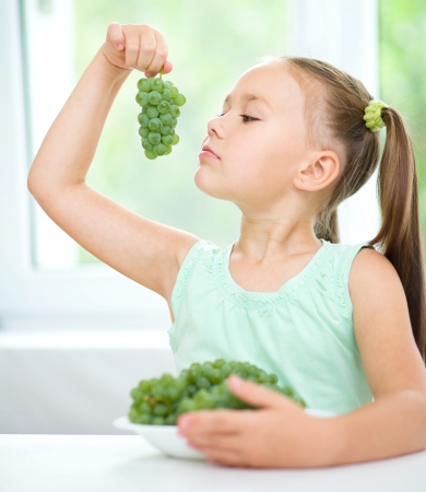 Cute little girl is eating green grapes, isolated over whiteの写真素材