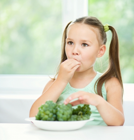 Cute little girl is eating green grapes, isolated over whiteの写真素材