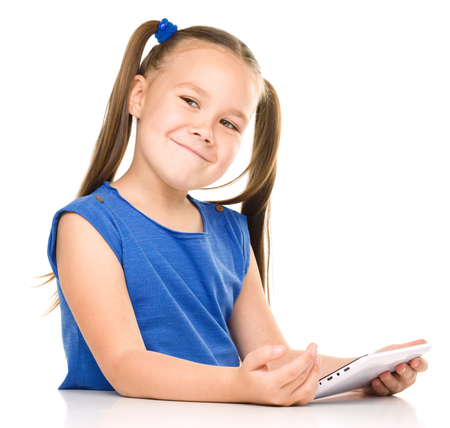 Young cheerful girl is using tablet while sitting at table, isolated over whiteの写真素材