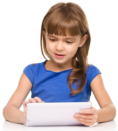 Young girl is using tablet while sitting at table, isolated over whiteの写真素材