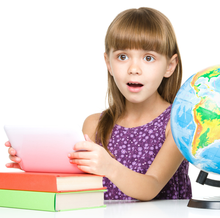 Surprised young girl is using tablet while studying geography, isolated over whiteの写真素材