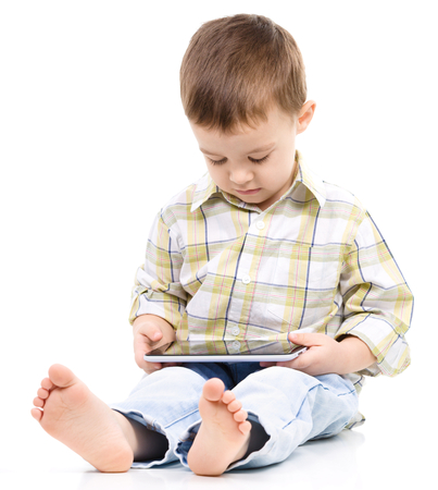 Young boy is using tablet while sitting on floor, isolated over whiteの写真素材