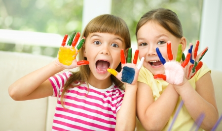Little girls are painting with gouache and showing their painted hands while sitting at tableの写真素材