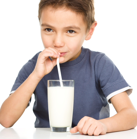Cute boy drinks milk using drinking straw, isolated over whiteの写真素材