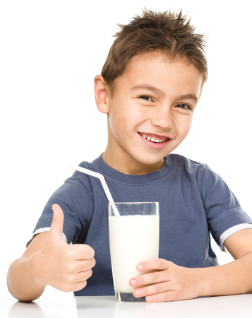 Cute boy drinks milk using a drinking straw while showing thumb up sign, isolated over whiteの写真素材