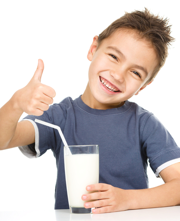 Cute boy drinks milk using a drinking straw while showing thumb up sign, isolated over whiteの写真素材