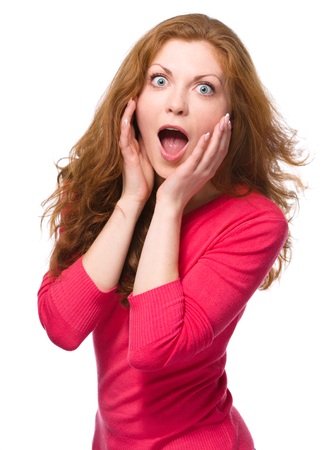 Young woman is holding her face in astonishment, isolated over whiteの写真素材